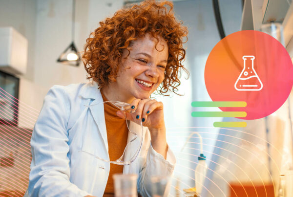 A scientist wearing a white lab coat who has curly red hair smiles