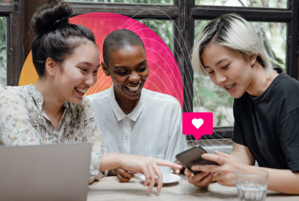 Earnings Conference Call Announcement;Three women sit at a table with a laptop looking at a smartphone