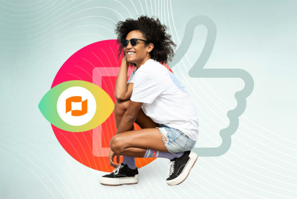 A woman with dark curly hair, a white T-shirt, denim shorts, black and white sneakers and black sunglasses