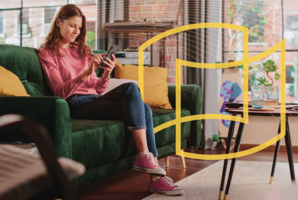 A woman in a pink sweater and jeans scrolls on her phone on an emerald green couch; transparent IZEA logo with yellow outline
