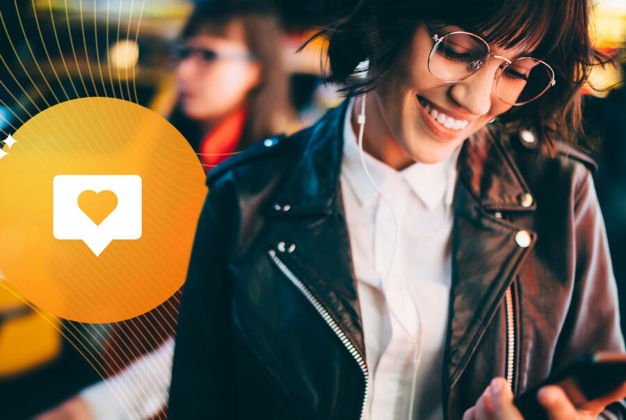 A woman wearing a leather jacket and white blouse and glasses smiles as she looks at her phone