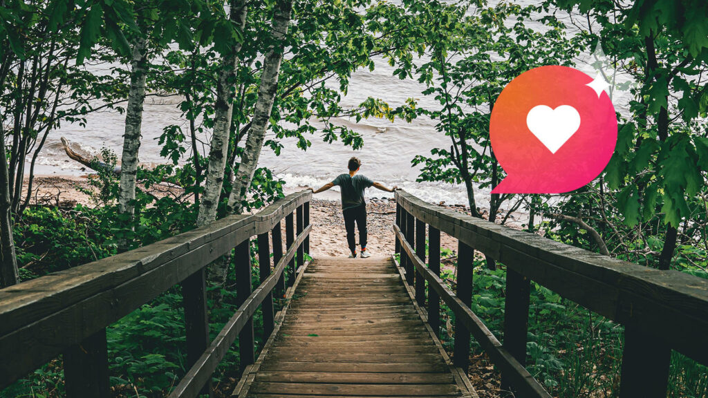 A person stands at the end of a walkway next to a lake