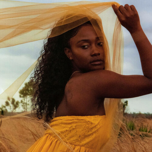 A woman in a yellow dress poses in a field