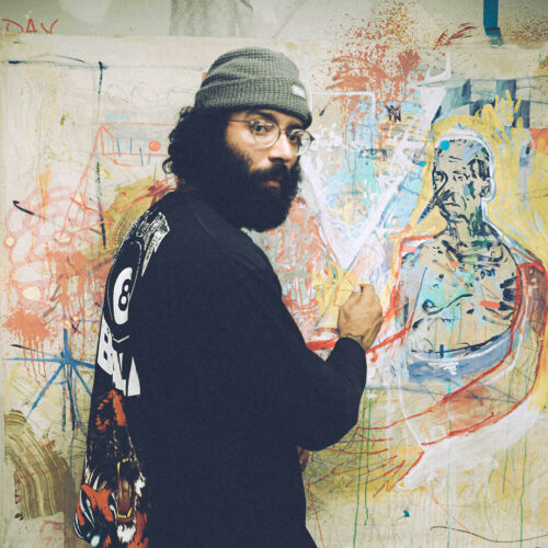 An artist paints a colorful image, looking back at the camera