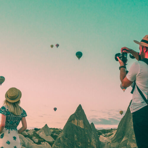 Two travelers take photos with hot air balloons in the air