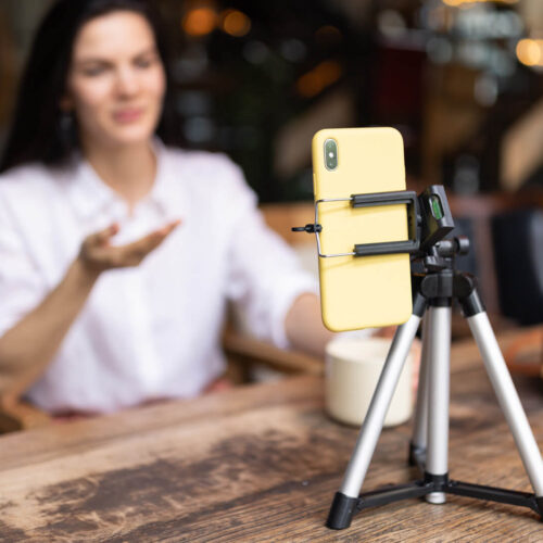 A woman films a video on her phone, which is on a mini tripod on a desk
